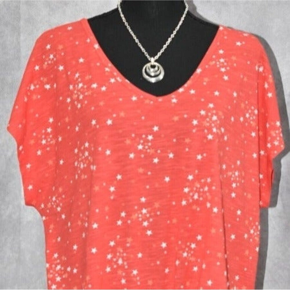 A coral red short-sleeve V-neck top with a white star pattern, displayed on a black mannequin torso with a silver pendant necklace.