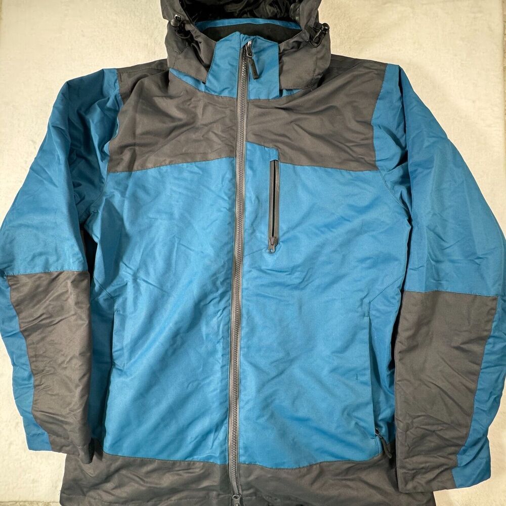 A blue and gray colorblock hooded jacket with a full front zipper and a vertical zippered chest pocket, laid flat against a light beige background.