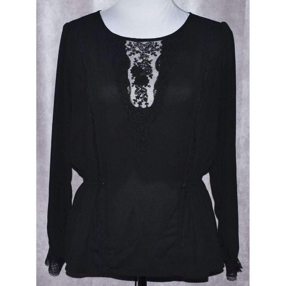 A black long-sleeve blouse with a sheer lace V-neckline panel, displayed on a white mannequin torso against a gray textured backdrop.