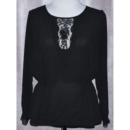 A black long-sleeve blouse with a sheer lace V-neckline panel, displayed on a white mannequin torso against a gray textured backdrop.