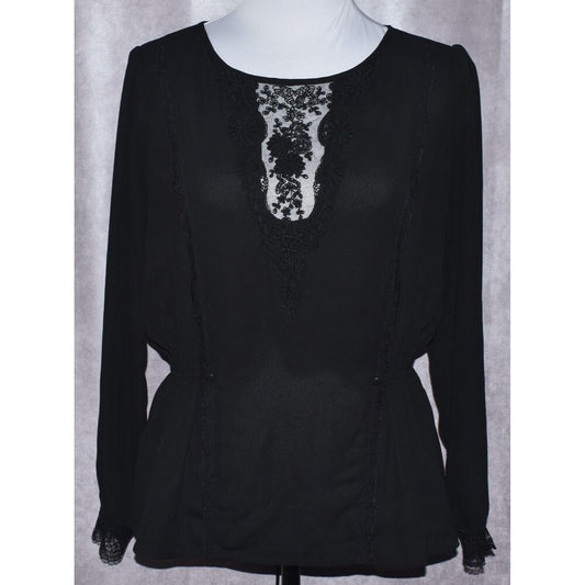 A black long-sleeve blouse with a sheer lace V-neckline panel, displayed on a white mannequin torso against a gray textured backdrop.