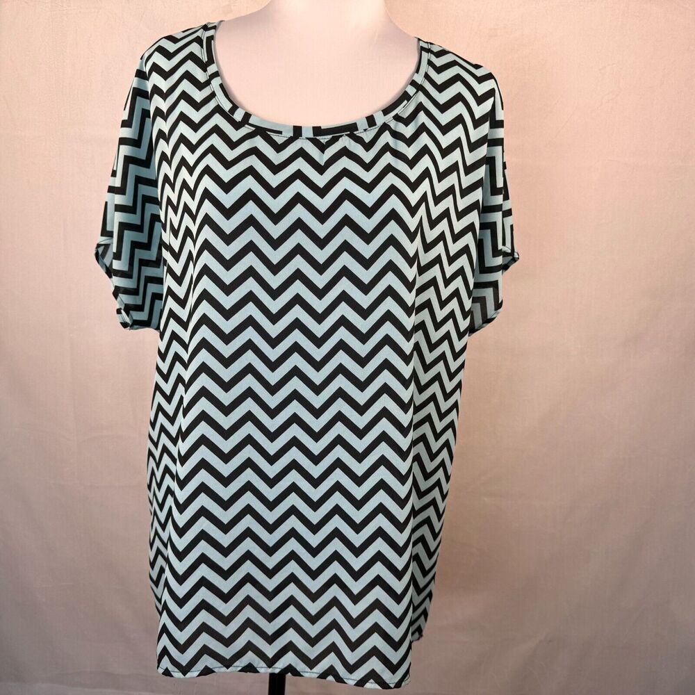 A short-sleeve scoop-neck top with a black and white chevron pattern, displayed on a mannequin against a light beige fabric backdrop.