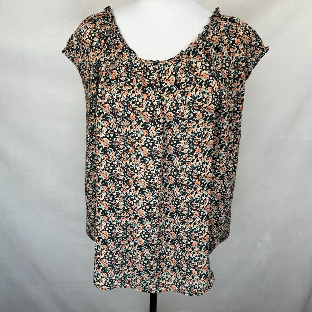 A women's short-sleeve blouse with a dense floral print, displayed on a white mannequin torso against a light gray fabric backdrop.
