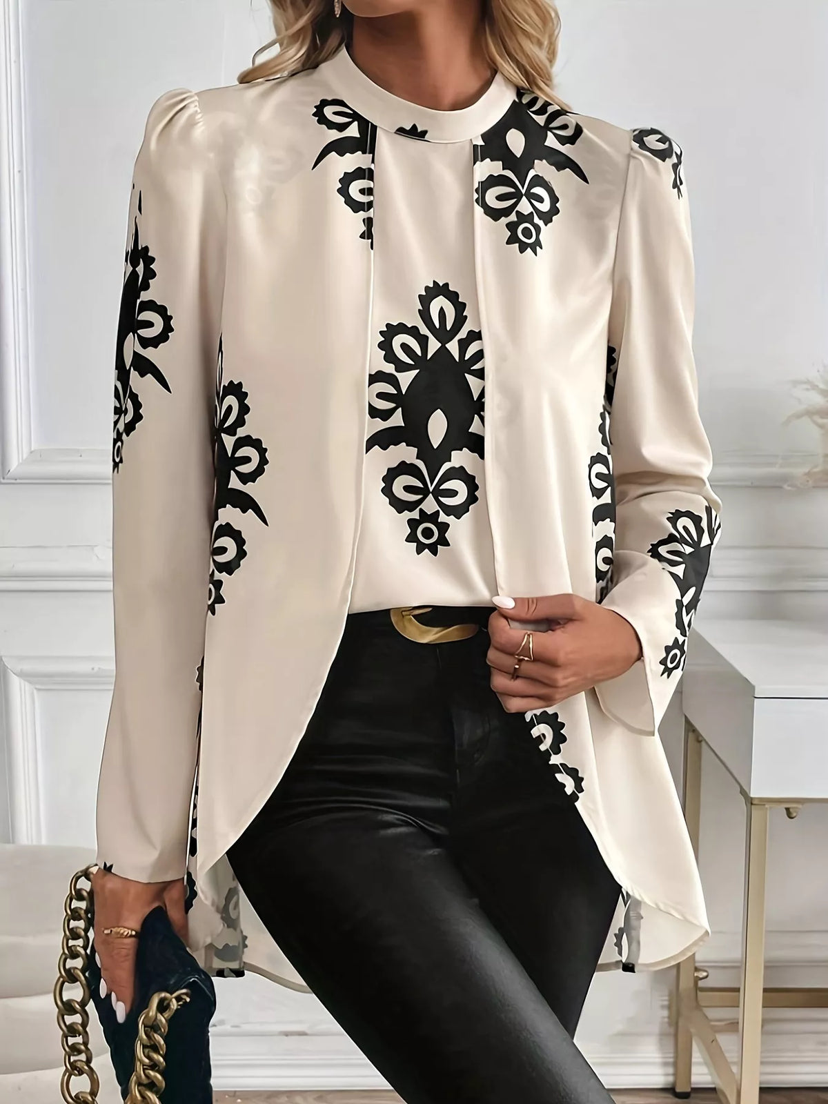 Woman wearing a cream Simply Love long sleeve blouse with black ornamental print and button front, styled with black pants.