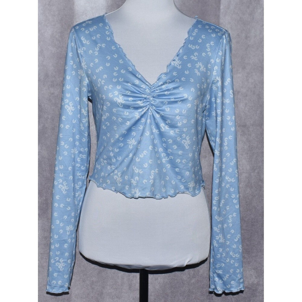 A light blue long-sleeve top with a white anchor pattern, displayed on a white mannequin torso against a gray textured background.