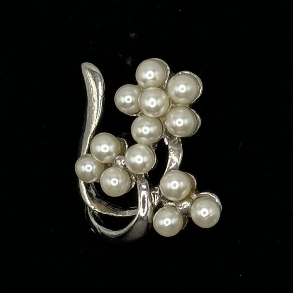 A silver-toned ring featuring a cluster of white faux pearls arranged in floral and vine-like patterns, set against a solid black background.