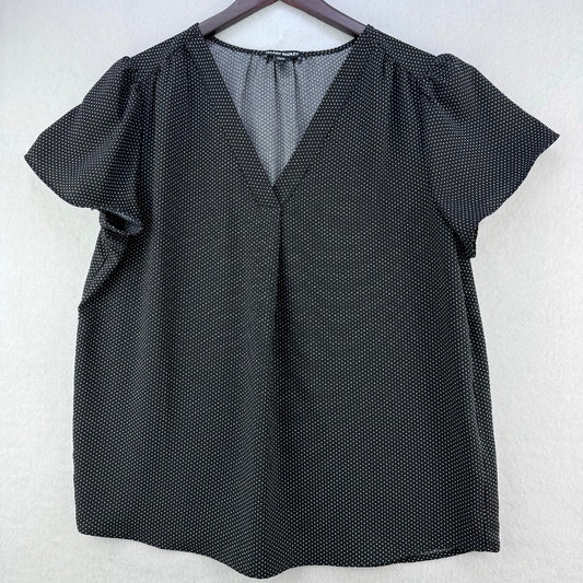 A black short-sleeve blouse with a subtle white polka dot pattern, featuring a V-neckline and puff sleeves, hanging on a dark wooden hanger against a light gray textured wall.