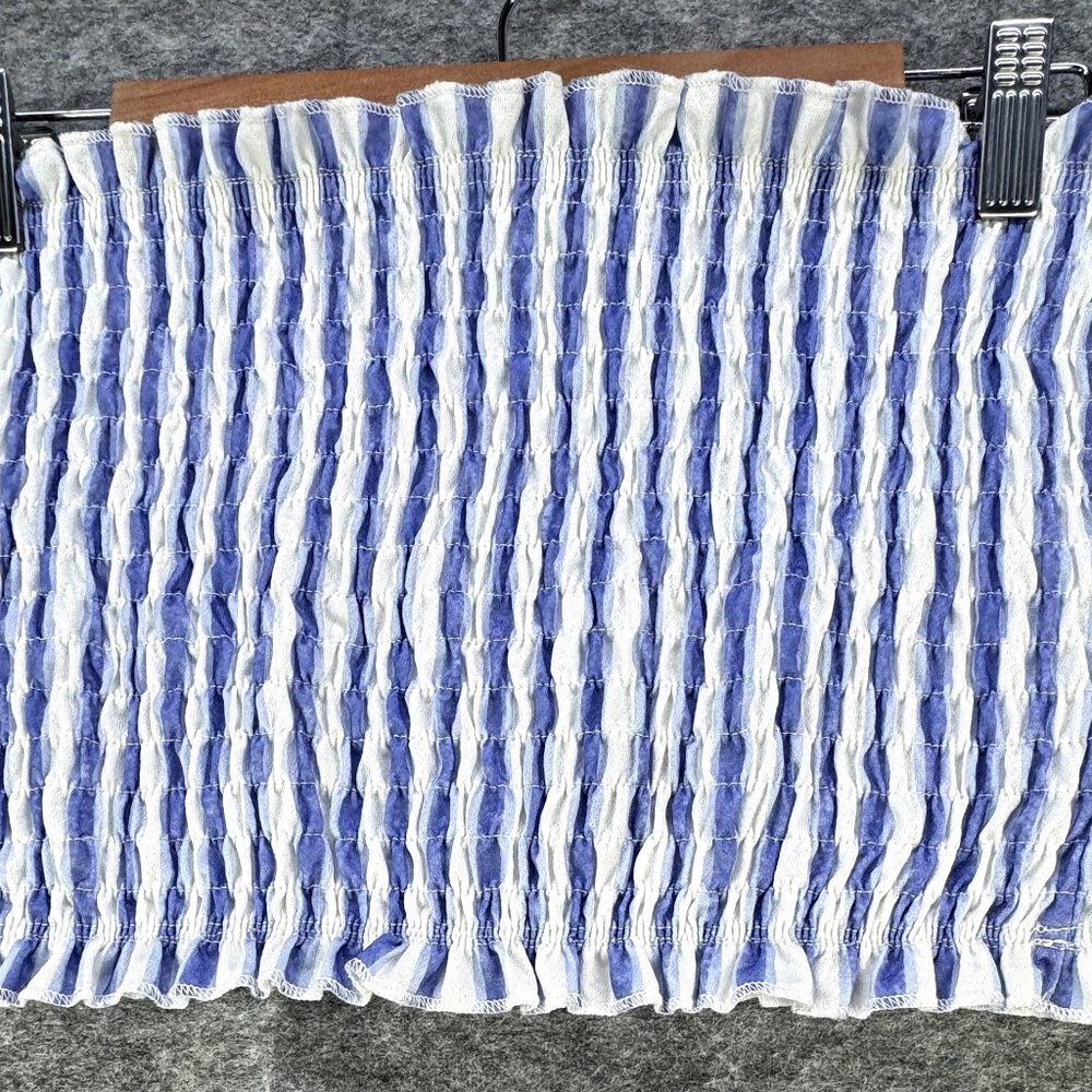 A smocked fabric panel with vertical ruching in blue and white, shown hanging from metal clips on a wooden hanger against a gray textured background.
