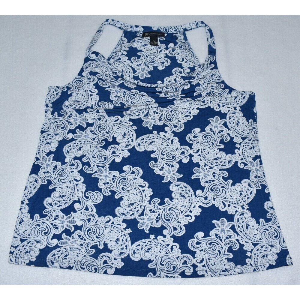 A women's sleeveless racerback tank top with a white floral and paisley lace-like pattern on a dark blue background, laid flat on a light gray surface.