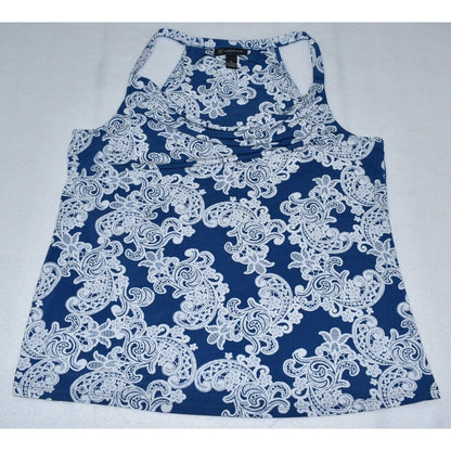 A women's sleeveless racerback tank top with a white floral and paisley lace-like pattern on a dark blue background, laid flat on a light gray surface.