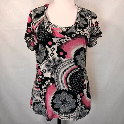 A short-sleeve scoop-neck blouse with a black, white, and pink paisley and floral pattern, displayed on a mannequin torso against a light gray fabric backdrop.