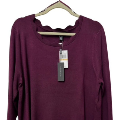 A long-sleeve scoop-neck knit top in deep plum purple, hanging on a beige hanger with retail tags attached against a plain white background.