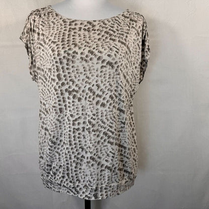 A short-sleeve scoop-neck blouse with an abstract leopard-like spot pattern in beige, brown, and gray, displayed on a mannequin torso against a light gray wall.