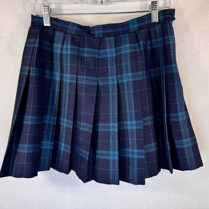 A pleated plaid mini skirt in navy blue with teal and light blue stripes, hanging from a clear plastic hanger against a light textured wall.