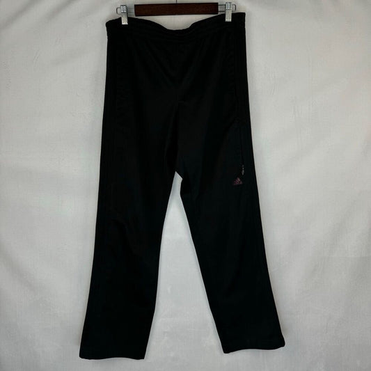 Black athletic pants hanging from a wooden hanger against a white fabric background, featuring a small red Adidas logo on the left leg.