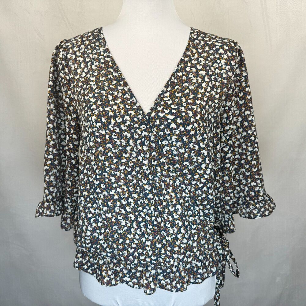 A women's short-sleeve blouse with a dark brown, white, and light blue floral pattern, displayed on a white mannequin torso against a neutral light gray background.