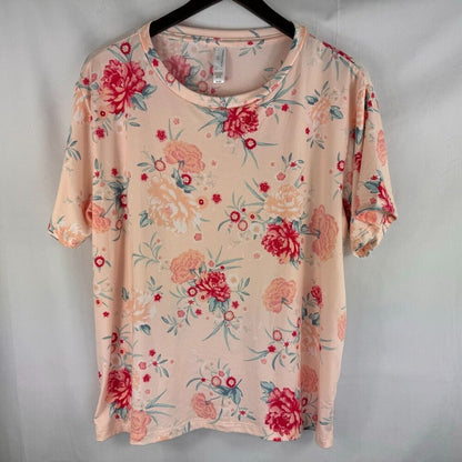 A short-sleeve crewneck blouse with a pinkish-beige base and a red, pink, and green floral print, hanging on a black hanger against a light gray backdrop.