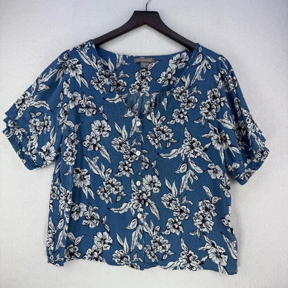 A women's short-sleeve blouse with a blue base and a white floral print, hanging on a black hanger against a light gray textured wall.