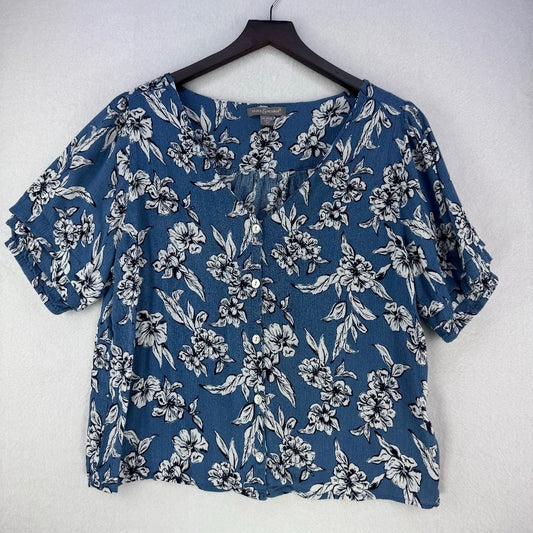 A women's short-sleeve blouse with a blue base and a white floral print, hanging on a black hanger against a light gray textured wall.