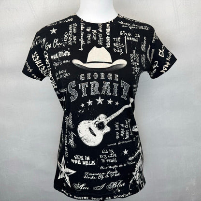 A black short-sleeve t-shirt displayed on a white mannequin torso against a light gray background. The shirt features a white graphic print with a cowboy hat, a guitar, and the text 'GEORGE STRAIGH' surrounded by handwritten-style text and stars.