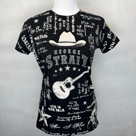 A black short-sleeve t-shirt displayed on a white mannequin torso against a light gray background. The shirt features a white graphic print with a cowboy hat, a guitar, and the text 'GEORGE STRAIGH' surrounded by handwritten-style text and stars.