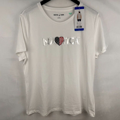 A white short-sleeve crewneck t-shirt by Nautica, featuring a 'N A T I C A' graphic across the chest with a heart in an American flag pattern. The shirt is hanging on a black hanger against a light gray fabric backdrop, with its retail hangtag still attached.