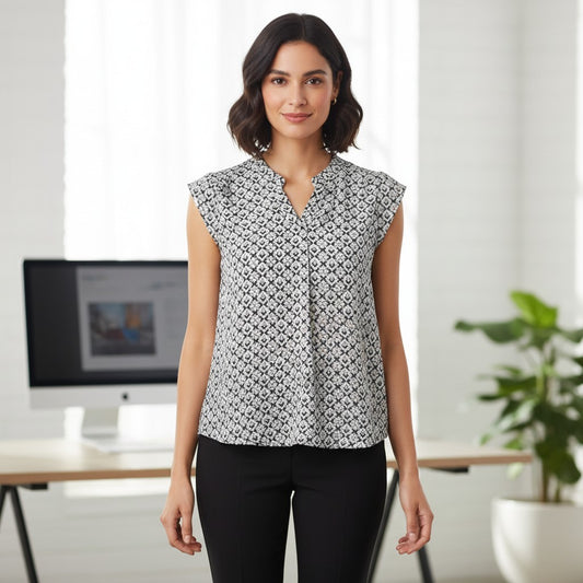 A woman modeling a sleeveless black and white geometric pattern blouse in an office setting.