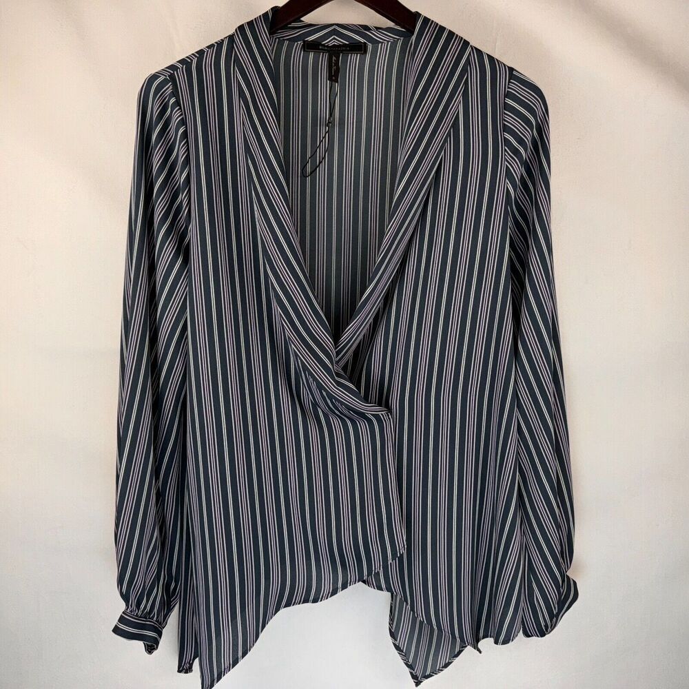 A long-sleeve wrap-style blouse with vertical navy, gray, and white stripes, hanging on a dark wooden hanger against a plain off-white fabric backdrop.