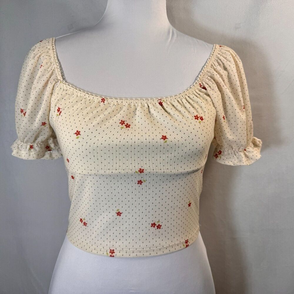 A cream-colored puff-sleeve crop top with a small red floral pattern, displayed on a white mannequin torso against a neutral gray background.