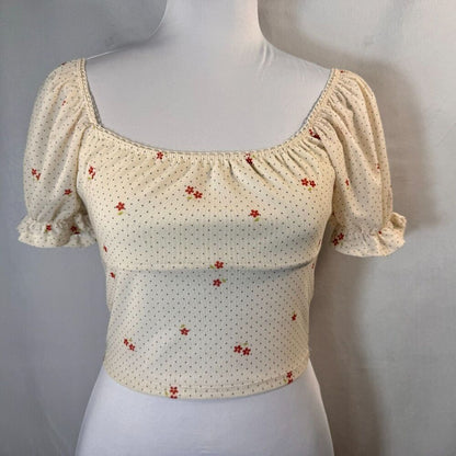 A cream-colored puff-sleeve crop top with a small red floral pattern, displayed on a white mannequin torso against a neutral gray background.