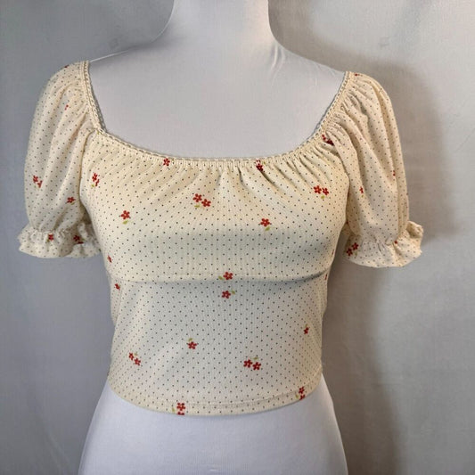 A cream-colored puff-sleeve crop top with a small red floral pattern, displayed on a white mannequin torso against a neutral gray background.