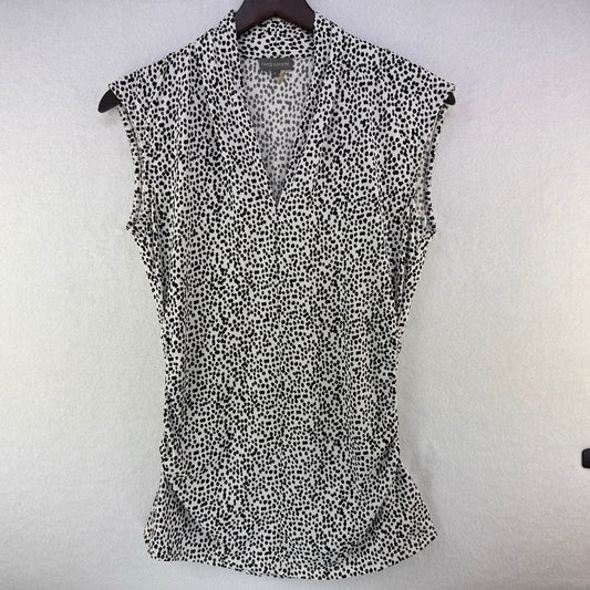 A sleeveless black and white spotted pattern blouse hanging on a dark hanger against a textured white wall.