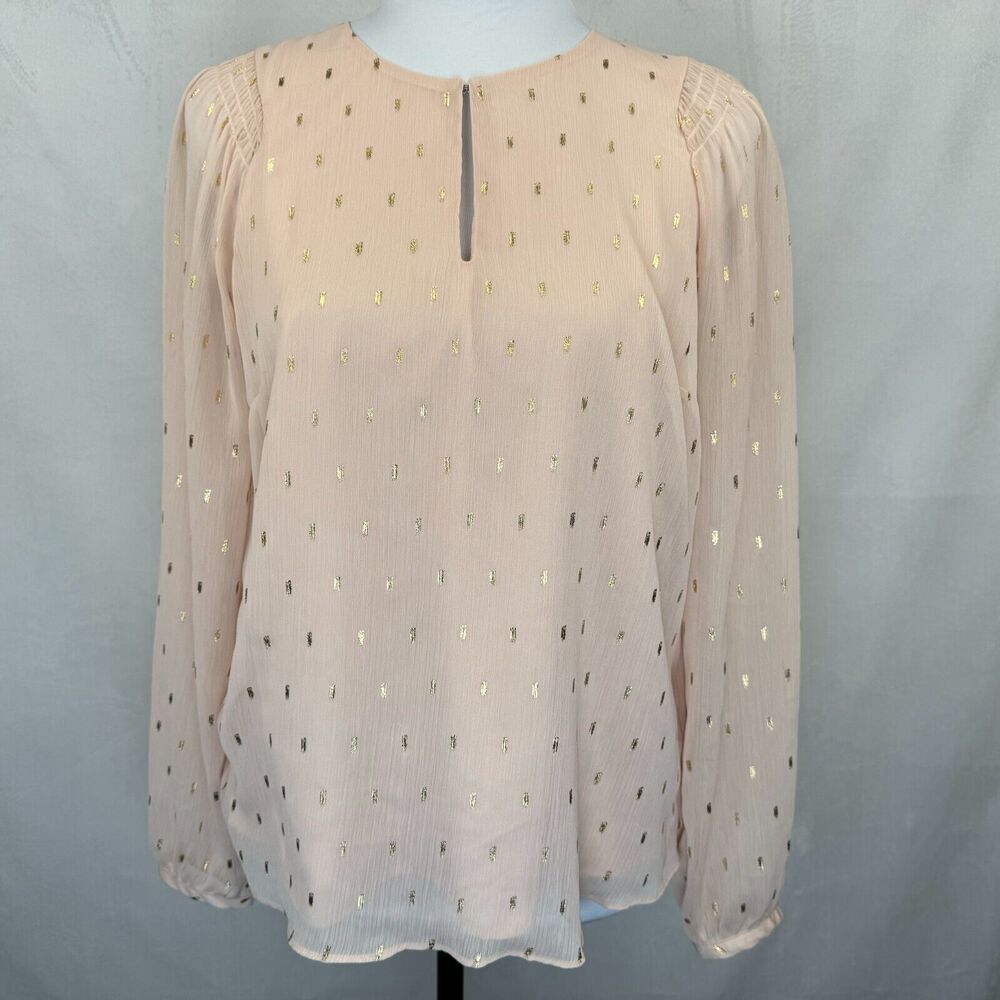 A pale blush pink sheer long-sleeve blouse with a subtle gold polka dot pattern, displayed on a mannequin torso against a light gray fabric backdrop.