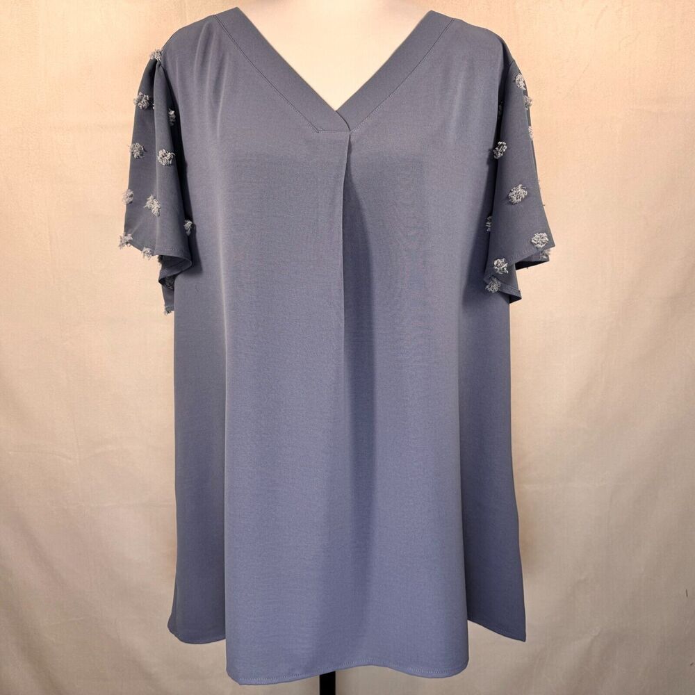 A slate blue V-neck tunic top displayed on a mannequin, featuring flutter sleeves with small white embroidered details.