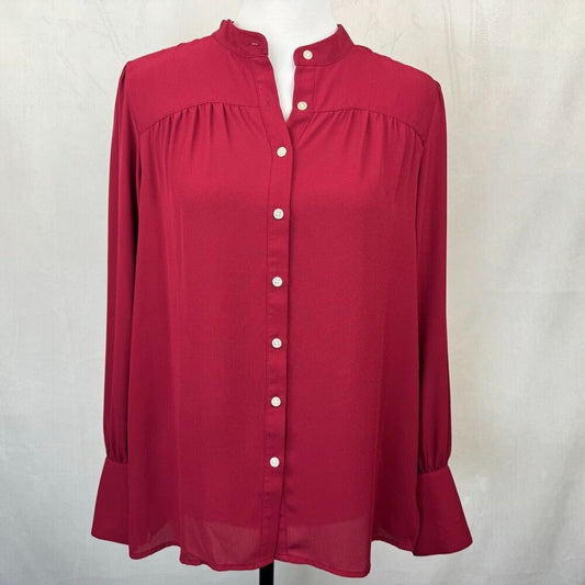 A long-sleeve blouse in deep red with a stand collar, gathered chest detailing, and a button-down front, displayed on a mannequin against a light gray fabric backdrop.