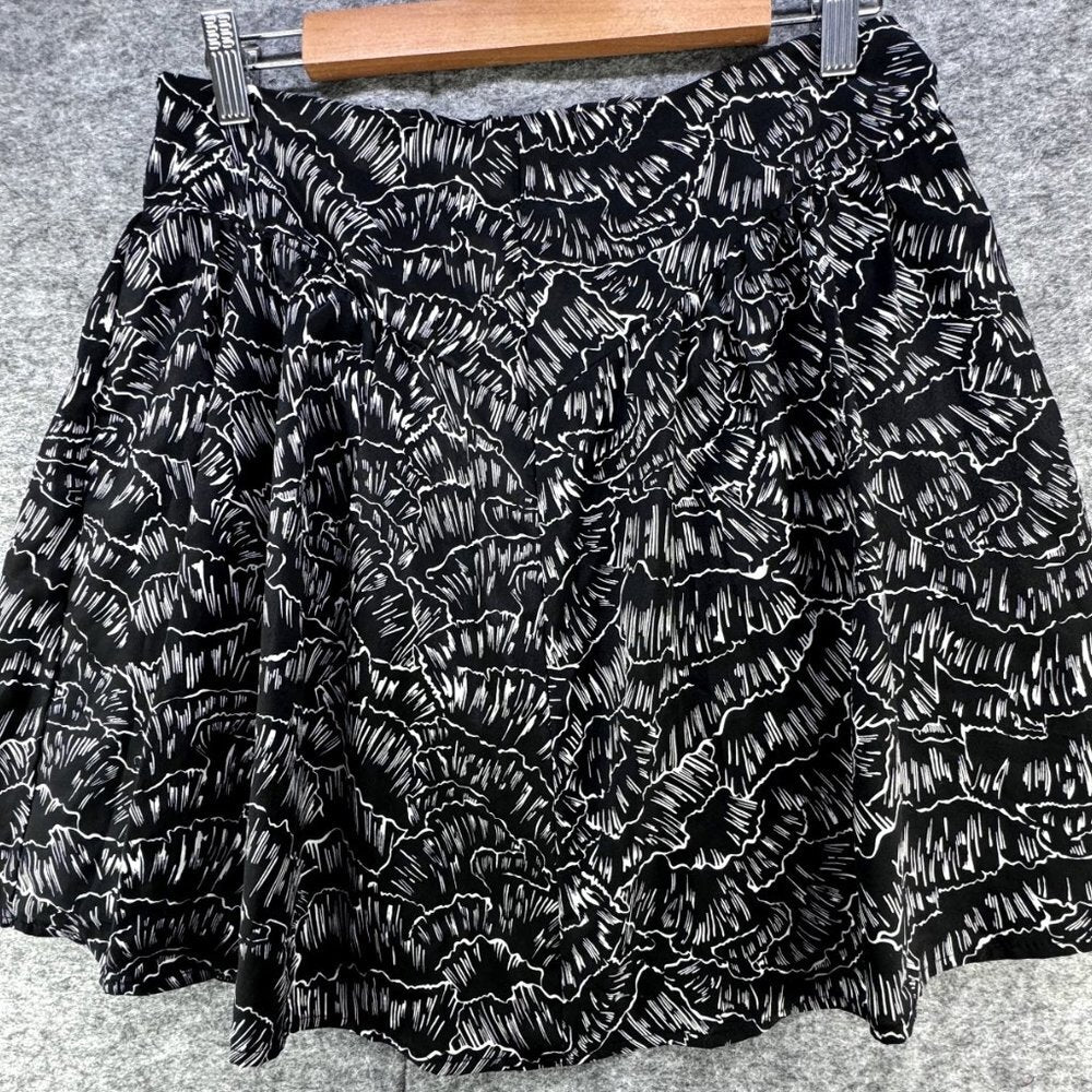 Black and white textured ruffled mini skirt with a flared silhouette, hanging on a wooden hanger against a gray felt background.