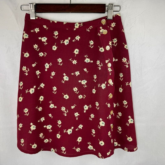 A burgundy A-line skirt with a small cream floral print, hanging on a dark wooden hanger against a textured white wall.