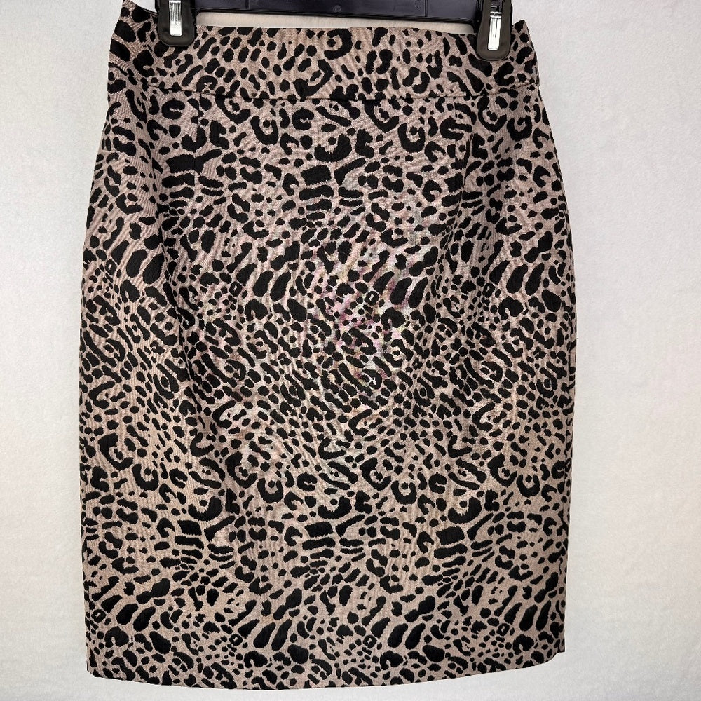 A leopard print pencil skirt in beige and black, hanging on a black hanger against a light gray textured wall.