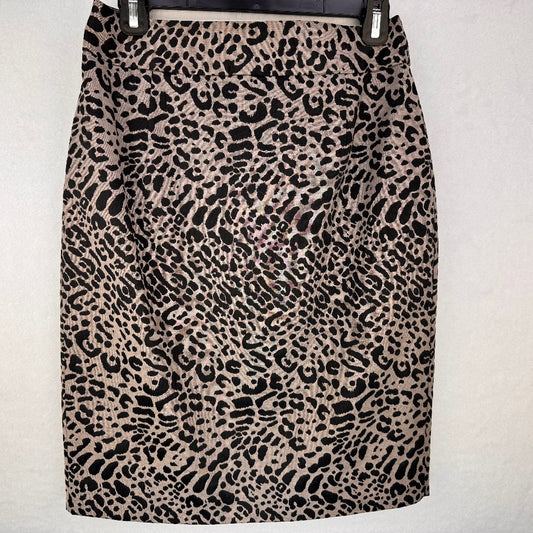 A leopard print pencil skirt in beige and black, hanging on a black hanger against a light gray textured wall.