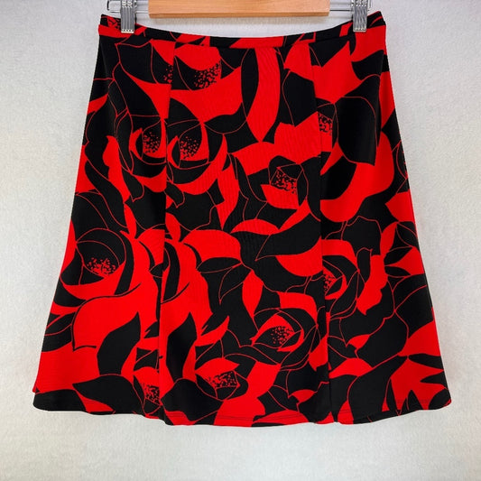 A red and black floral print A-line skirt hanging on a wooden hanger against a light textured wall.