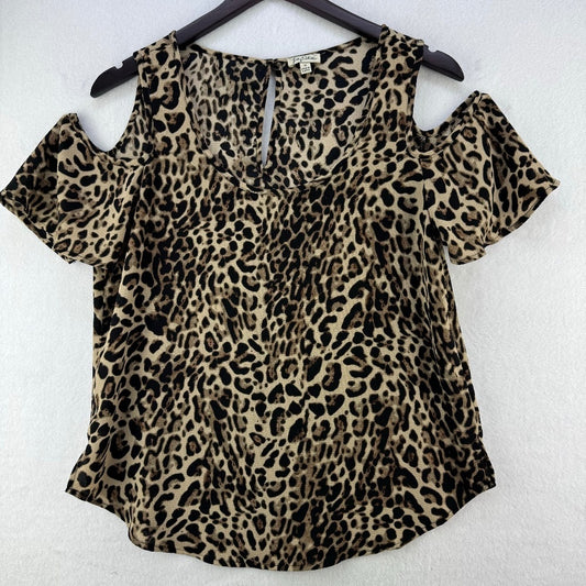 A leopard print cold-shoulder top hanging on a black hanger against a white textured wall. The top features a beige and brown base with black leopard spots and short puff sleeves.
