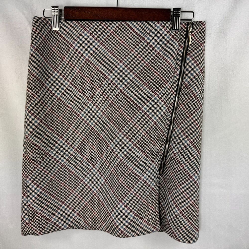 A women's wrap-style mini skirt with a diagonal black, white, and brown gingham pattern, featuring a black side zipper, hanging on a wooden hanger against a white fabric background.