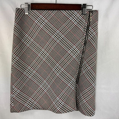 A women's wrap-style mini skirt with a diagonal black, white, and brown gingham pattern, featuring a black side zipper, hanging on a wooden hanger against a white fabric background.
