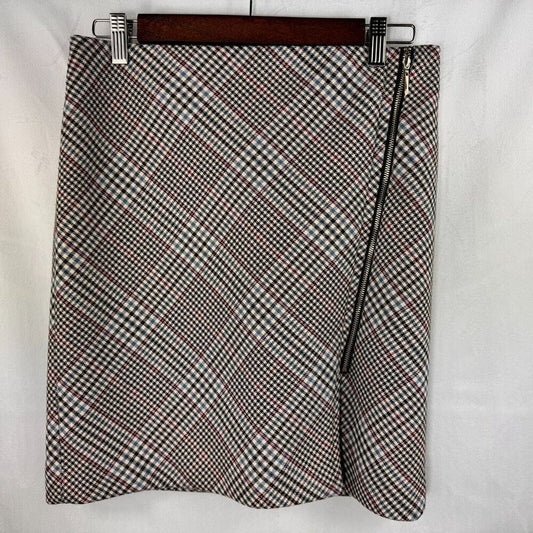 A women's wrap-style mini skirt with a diagonal black, white, and brown gingham pattern, featuring a black side zipper, hanging on a wooden hanger against a white fabric background.