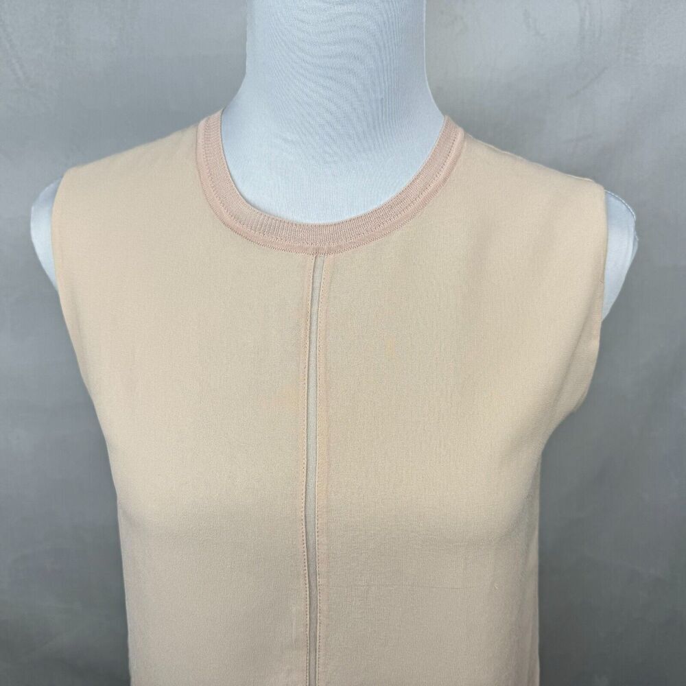 A sleeveless beige knit top displayed on a white mannequin torso against a textured gray background.