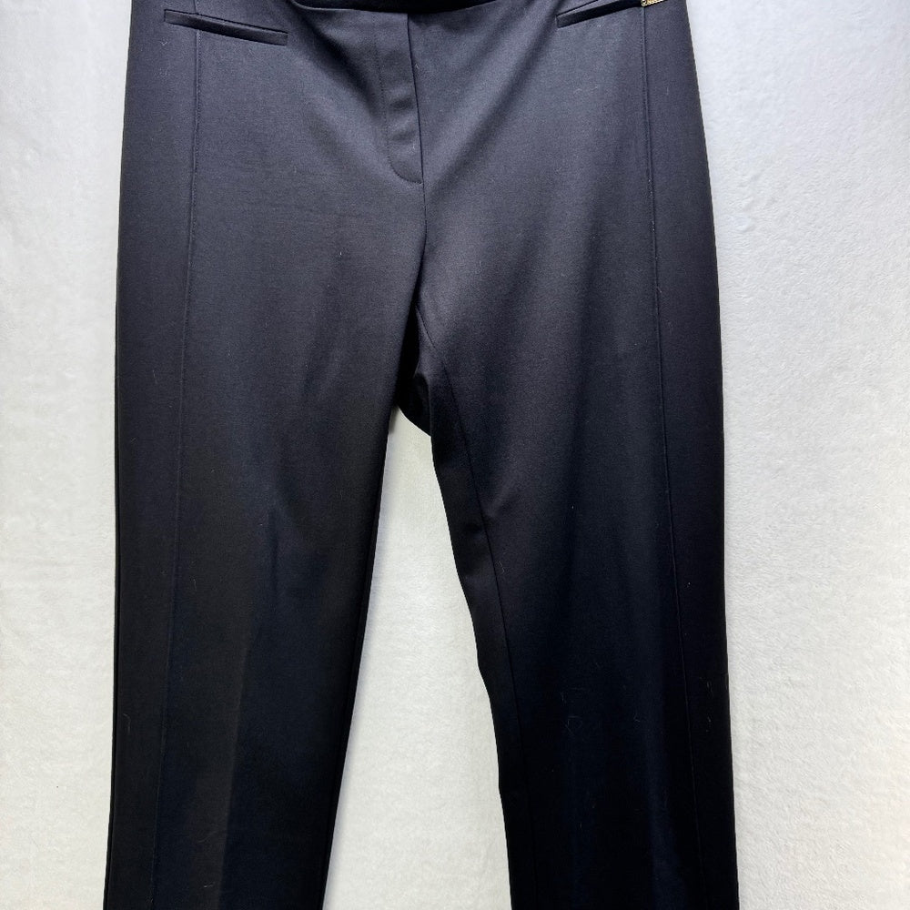 A pair of dark charcoal gray or black trousers hanging against a light gray textured wall.