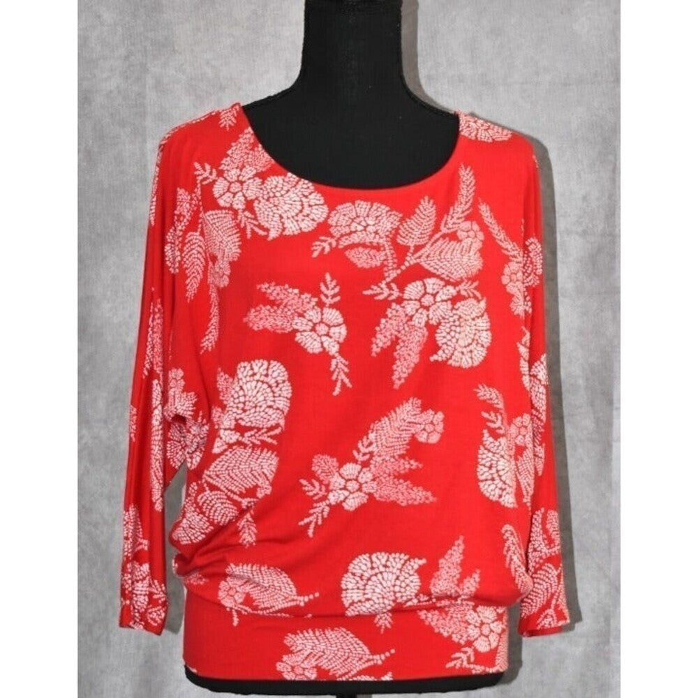 A red long-sleeve top with a white floral and leafy pattern, displayed on a black mannequin torso against a gray textured background.