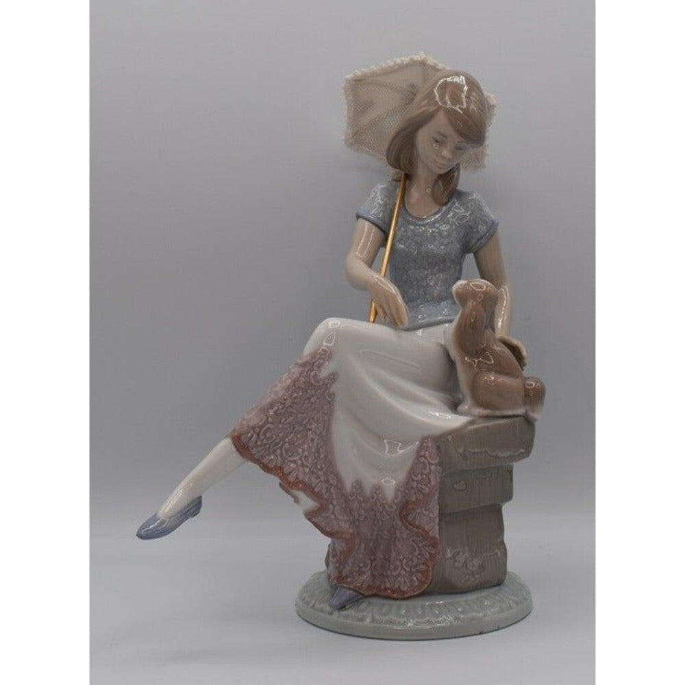 A porcelain figurine of a woman seated on a stool, holding a parasol, with a small rabbit beside her. The figurine is shown against a plain gray studio background.