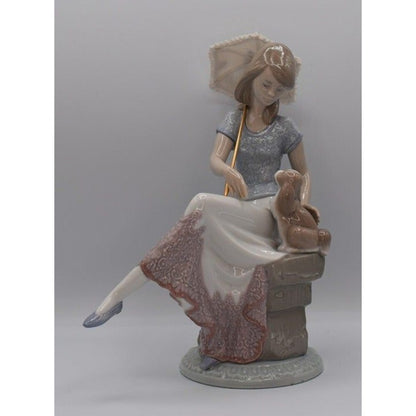 A porcelain figurine of a woman seated on a stool, holding a parasol, with a small rabbit beside her. The figurine is shown against a plain gray studio background.