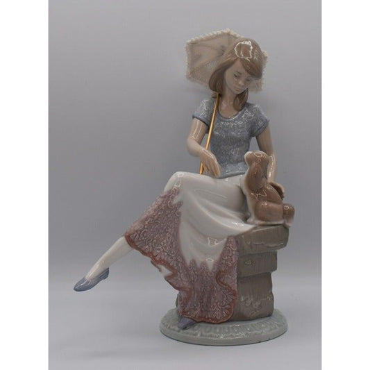 A porcelain figurine of a woman seated on a stool, holding a parasol, with a small rabbit beside her. The figurine is shown against a plain gray studio background.